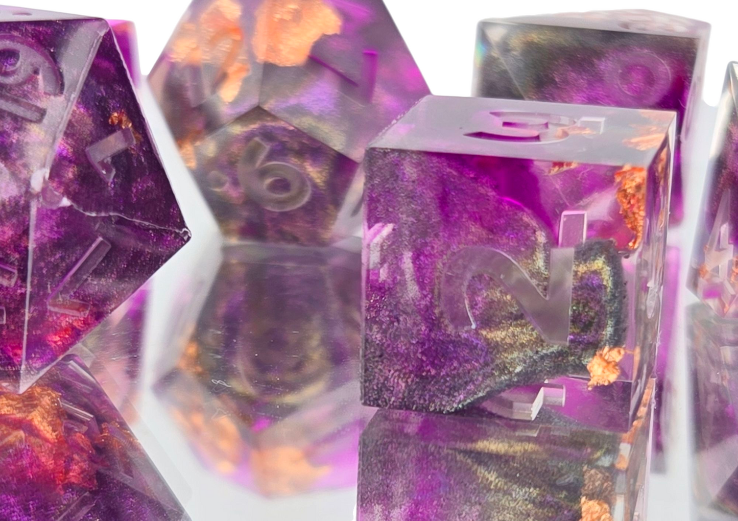 A closeup of a d6 with the remaining dice visible out of focus in the background. The are clear with swirled transparent purple and colorshifting purple shimmer, and occasional gold flakes.