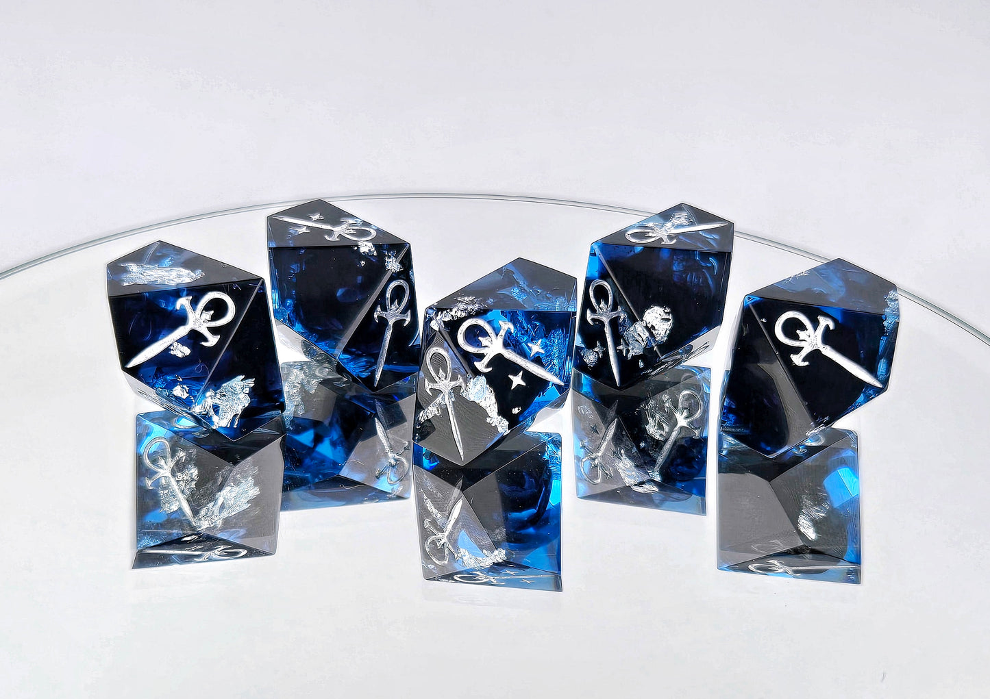 A set of 5 Vampire the Masquerade Hunger style dice. The dice are transparent blue with black ink and silver foil inside. The symbols are inked in silver.
