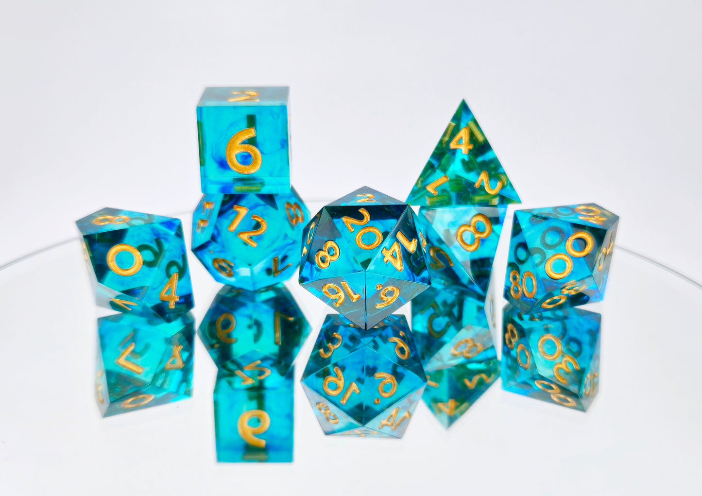 A full 7 piece polyhedral ttrpg dice set. The dice are transparent light teal blue with thin wisps of darker blue swirled inside and gold numbering.