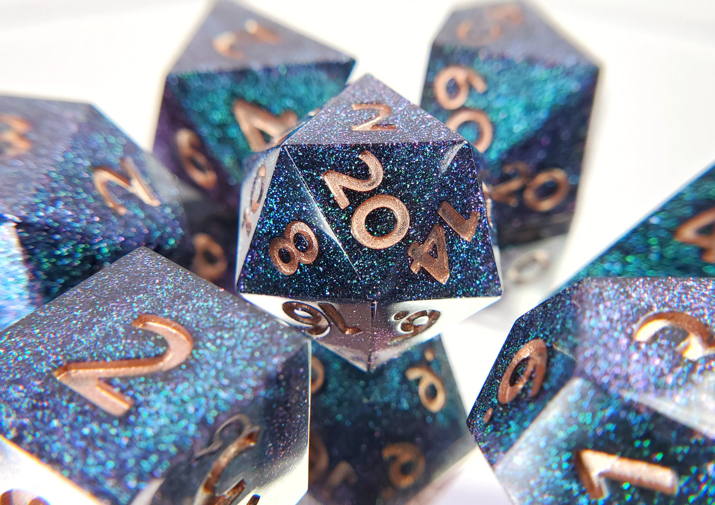 A full 7 piece polyhedral ttrpg dice set. The dice are densely packed blue and green colorshift glitter with rose gold inking for the symbols.