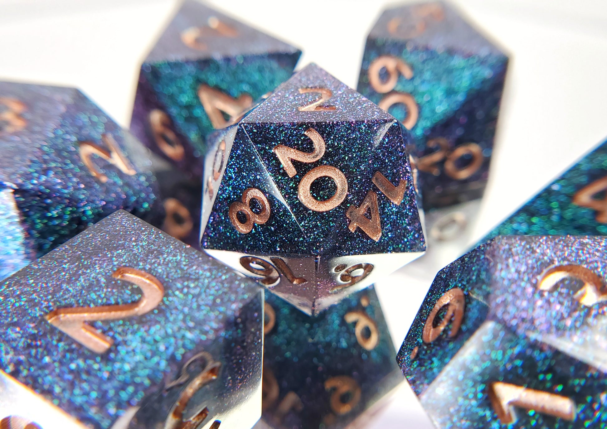 A full 7 piece polyhedral ttrpg dice set. The dice are densely packed blue and green colorshift glitter with rose gold inking for the symbols.