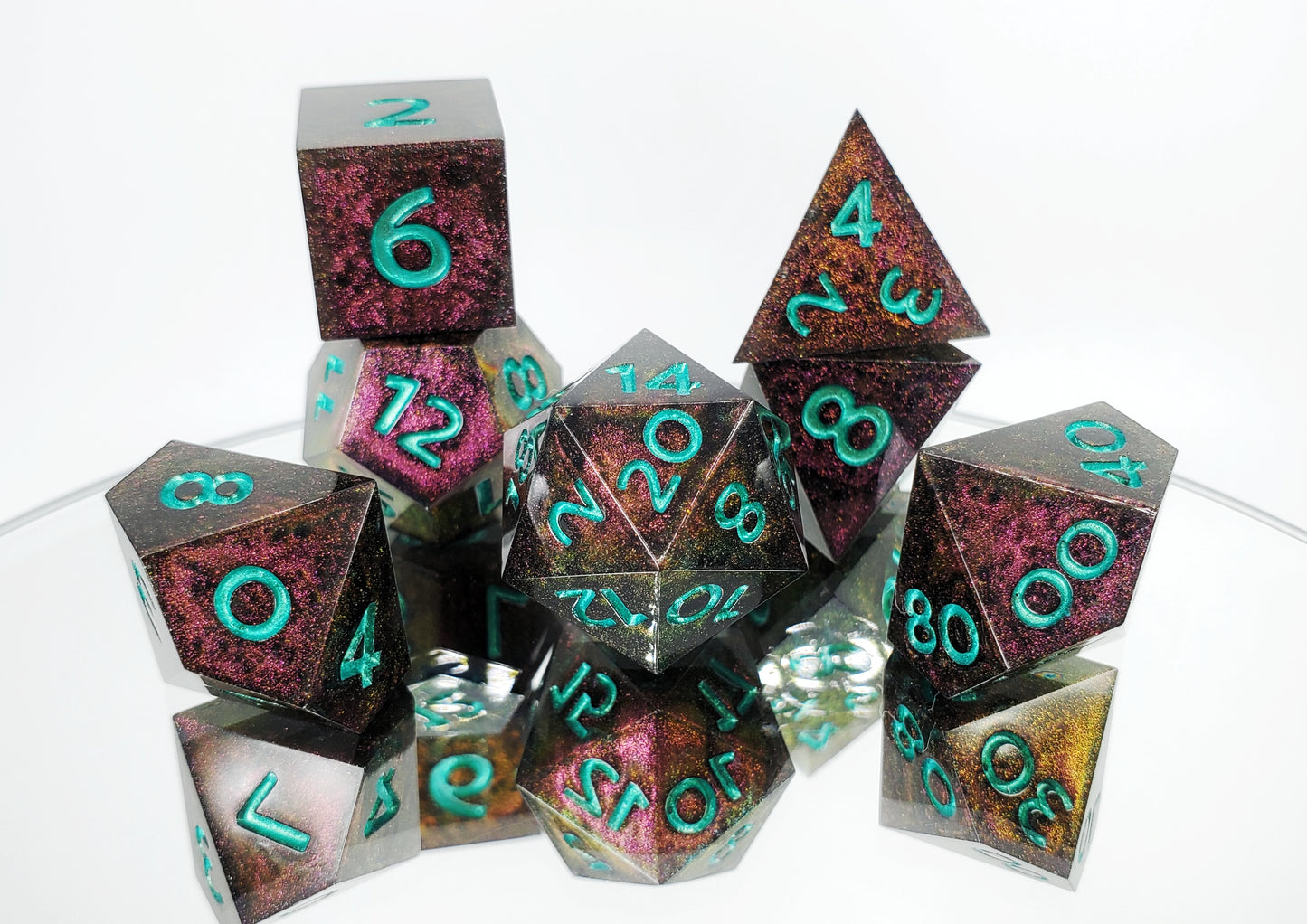 A full 7 piece polyhedral ttrpg dice set. The dice are a red/purple/yellow/green colorshift shimmer with metallic cool green numbering.