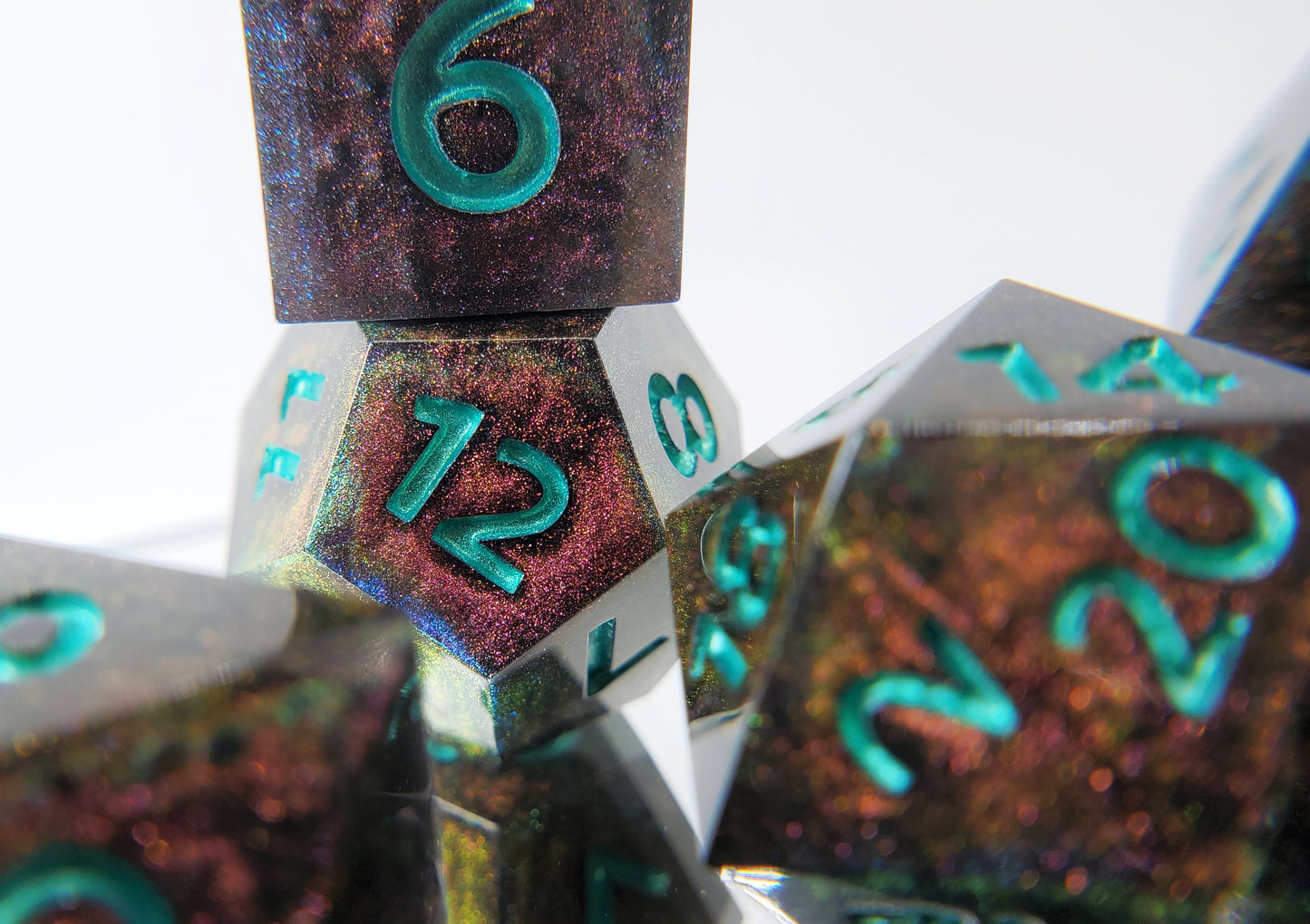 A close up of a d6 stacked on a d12 from a polyhedral ttrpg dice set. The dice are a red/purple/yellow/green colorshift shimmer with metallic cool green numbering.