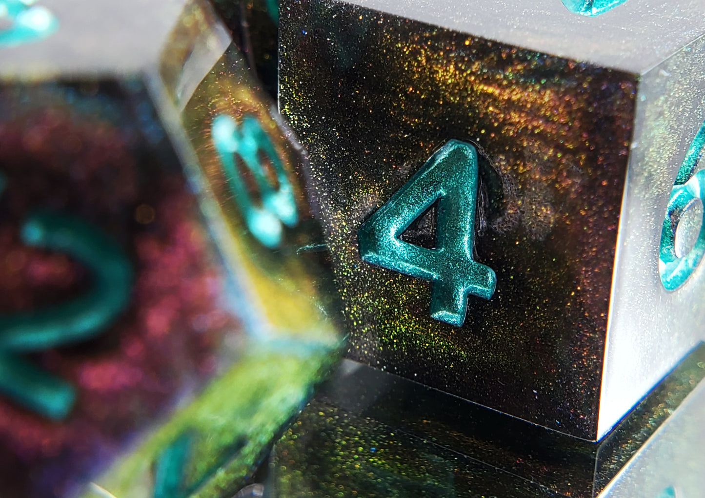 A closeup of a d6 from a ttrpg dice set. The dice are a red/purple/yellow/green colorshift shimmer with metallic cool green numbering.