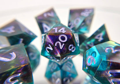 A 7 piece polyhedral ttrpg dice set. The dice are transparent light blue with ultrafine glitter sparkles, colorshift bloops, and light purple metallic numbers.