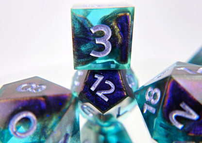 A closeup of a d6 stacked on a d12 from a ttrpg dice set. The dice are transparent light blue with ultrafine glitter sparkles, colorshift bloops, and light purple metallic numbers.