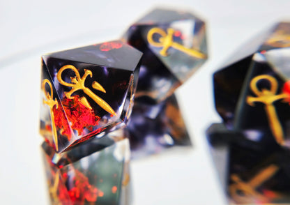 A closeup of a Vampire the Masquerade Hunger style d10. The dice are clear with black ink and red foil swirled within. The symbols are inked in gold.