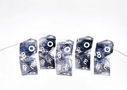 A 5d10 resin dice set. The dice are transparent clear with colorshifting glitter sparkles, black ink tendrils swirled inside, and pearl white numbers.