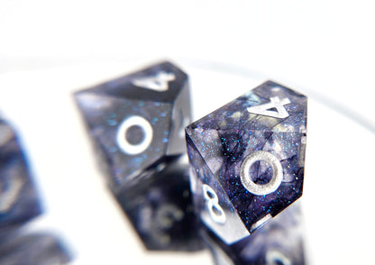 A closeup of a d10 from a 5d10 ttrpg dice set. The dice are transparent clear with colorshifting glitter sparkles, black ink tendrils swirled inside, and pearl white numbers.