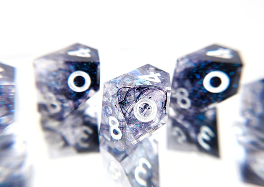 A cloesup of one d10 from a 5d10 ttrpg dice set. The dice are transparent clear with colorshifting glitter sparkles, black ink tendrils swirled inside, and pearl white numbers.