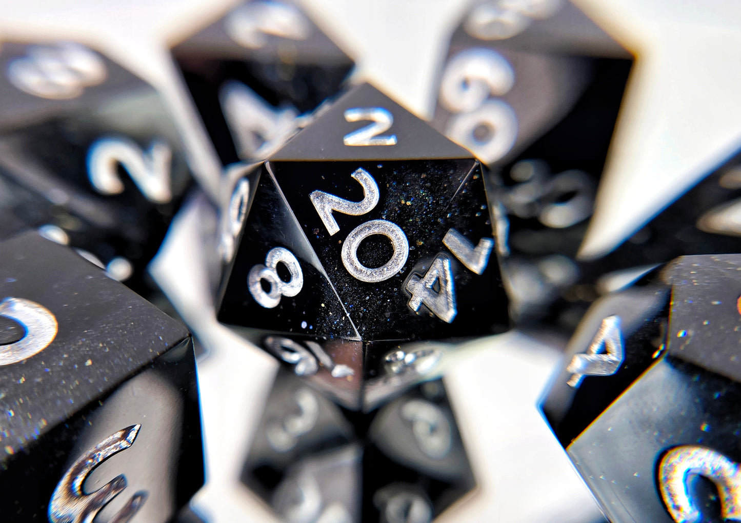 A 7 piece polyhedral ttrpg dice set. The dice are a swirl of plain black and shimmery black with bright silver numbers.