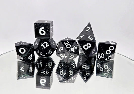 A 7 piece polyhedral ttrpg dice set. The dice are a swirl of plain black and shimmery black with bright silver numbers.