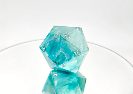 A jumbo sized d20 with swirls of white and icey ocean blues alongside super fine subtle glitter sparkles. The numbers are shrunken down and placed in the corners so that they are still readable but the design of the die is not covered.