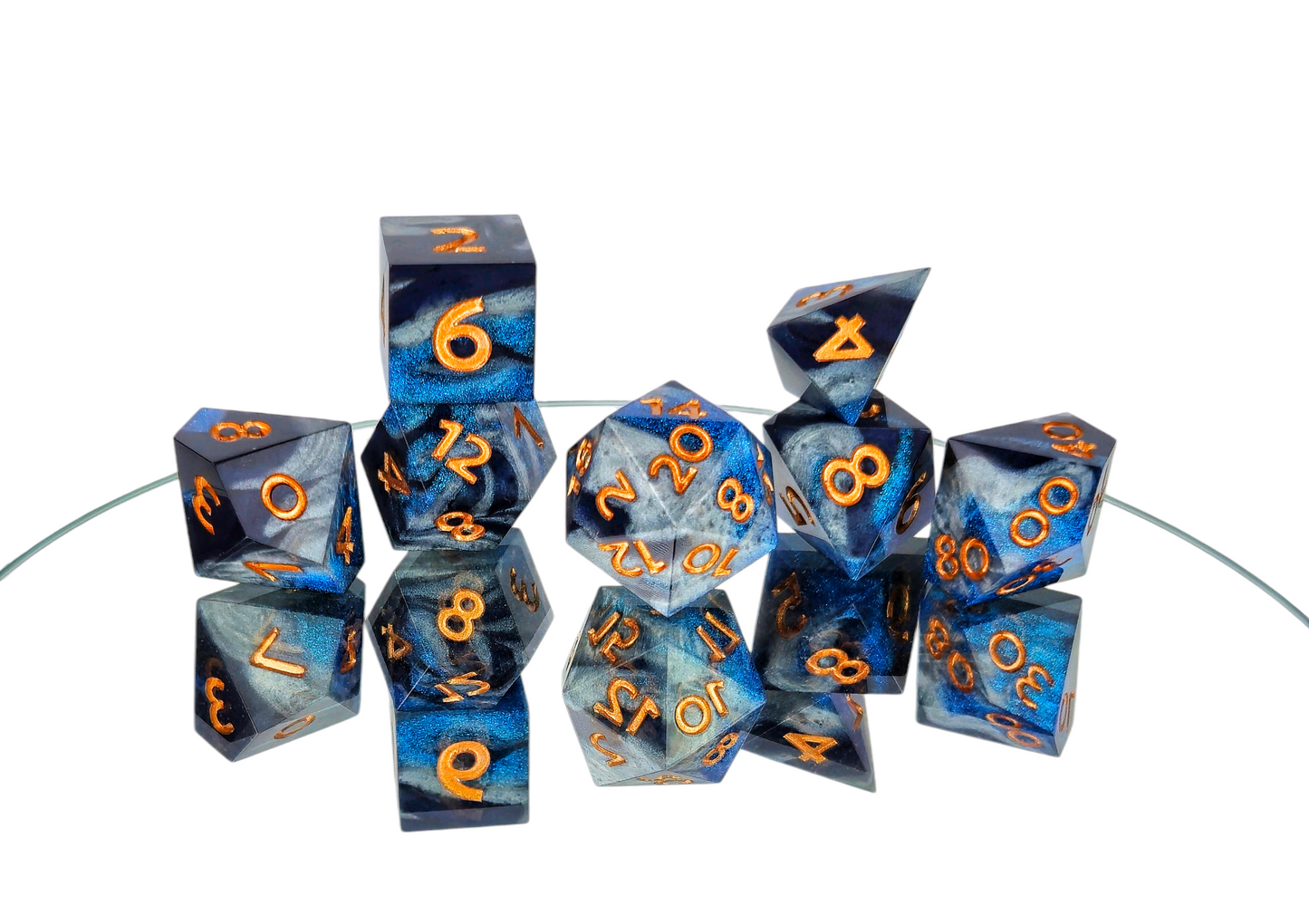 A 7 piece polyhedral ttrpg dice set. The dice are swirls of silver, shimmery navy, and shimmery bright blue with copper numbers.