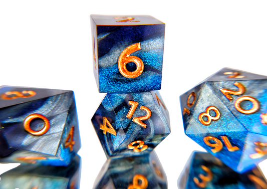 A closeup of a d6 stacked on a rhombic d12 from a ttrpg dice set. The dice are swirls of silver, shimmery navy, and shimmery bright blue with copper numbers.