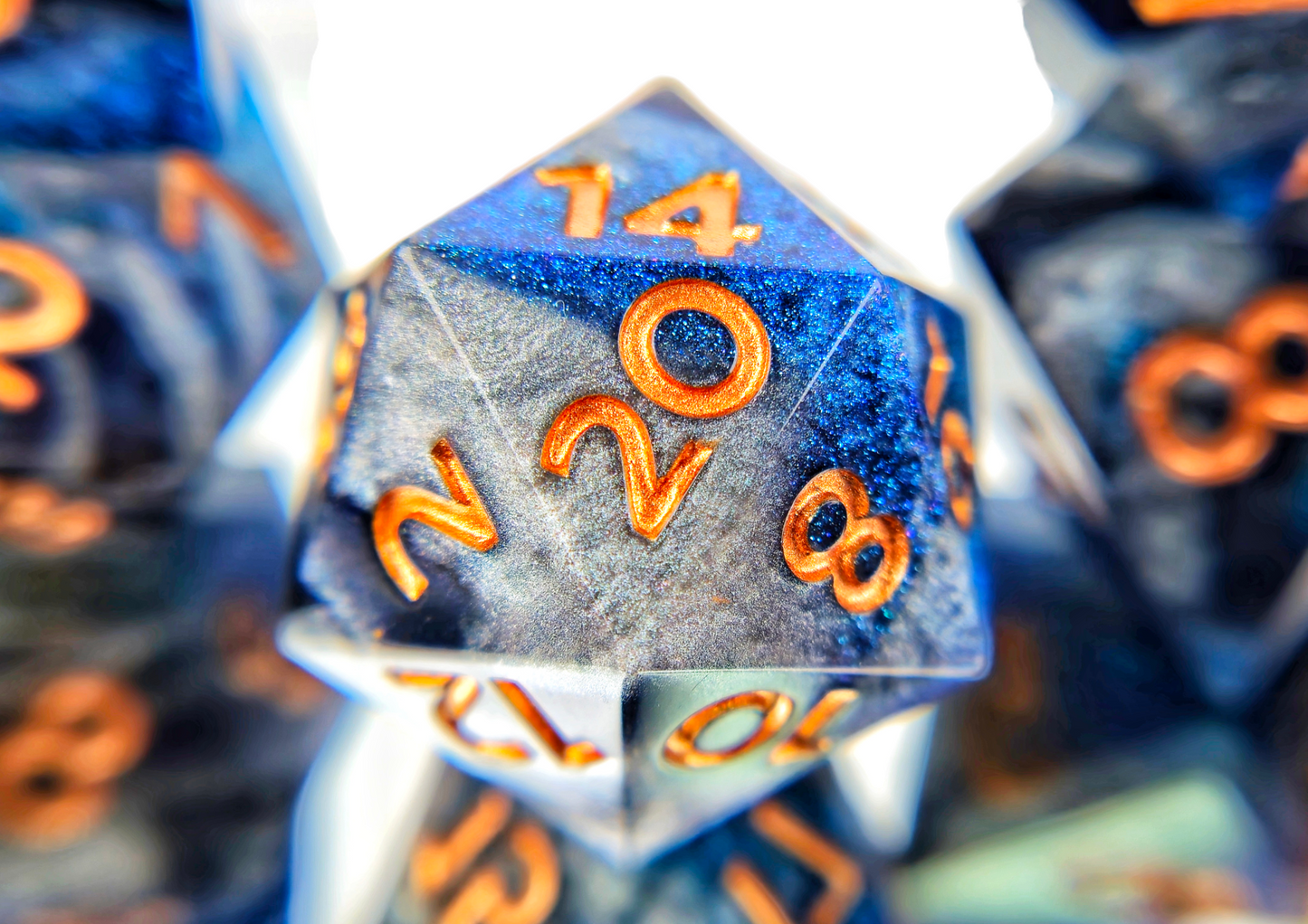 A closeup of a d20 from a ttrpg dice set. The dice are swirls of silver, shimmery navy, and shimmery bright blue with copper numbers.