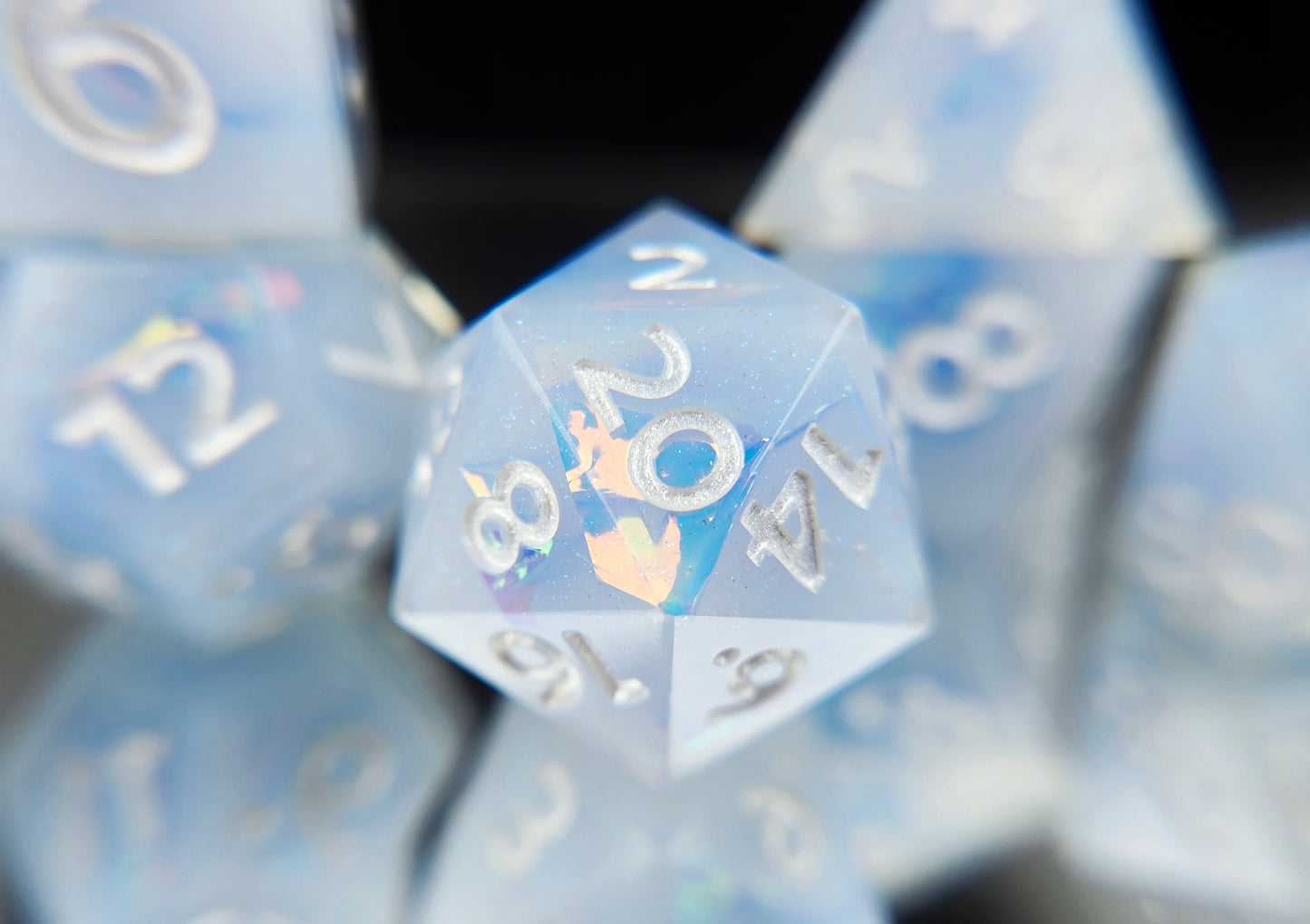 A closeup of a d20 from a ttrpg dice set. The dice are milky blue-ish white resin and blue/green sparkles with flashes of ice blue mylar peeking out and pearl white numbers.