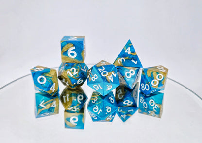 A 7 piece polyhedral ttrpg dice set. The dice are swirled metallic teal and gold with pearl white numbers.