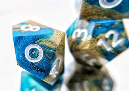 A closeup of a d10 from a ttrpg dice set. The dice are swirled metallic teal and gold with pearl white numbers.