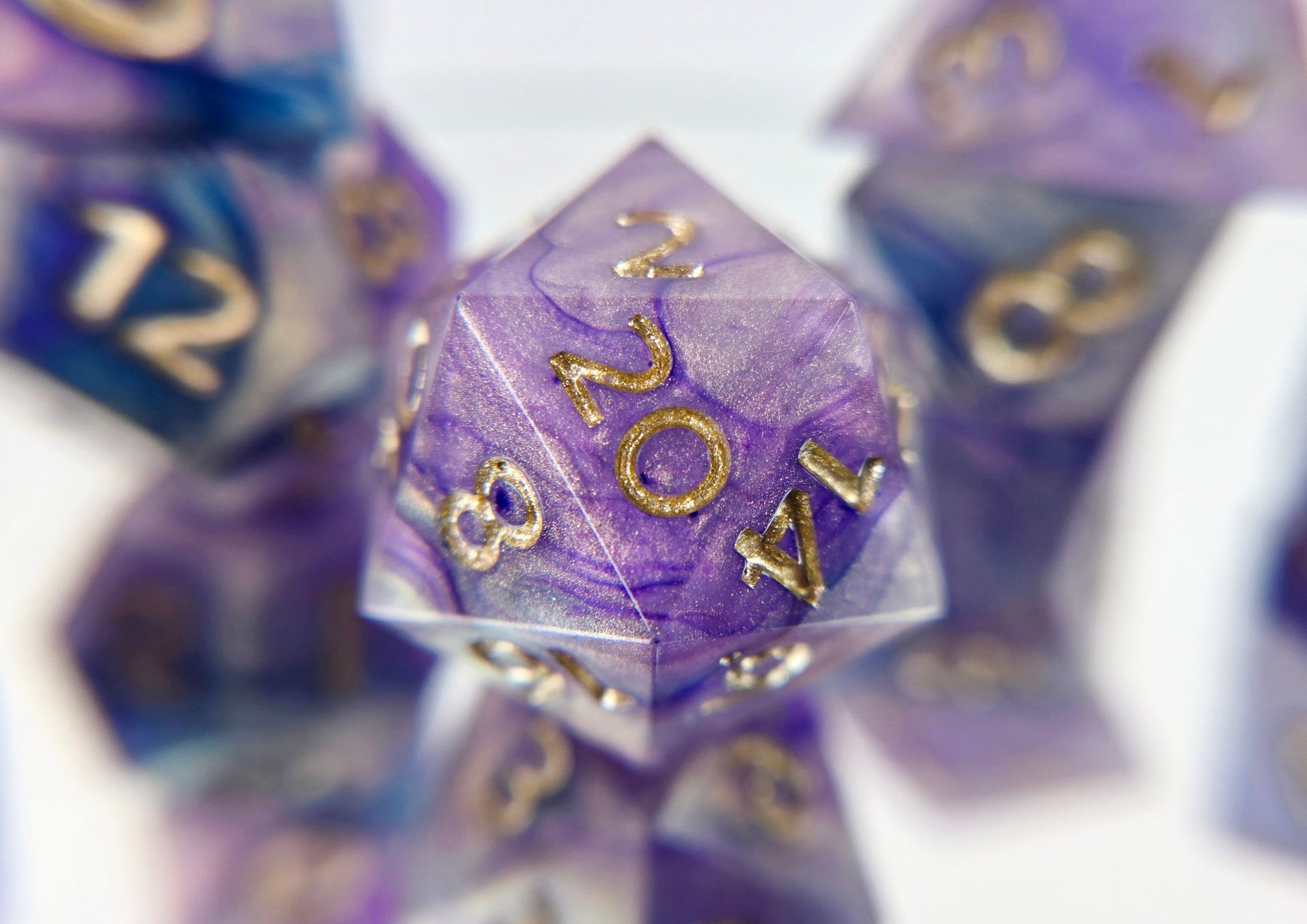 A closeup of a d20 from a ttrpg dice set. The dice are a warm pearlescent base with purple and navy ink swirled over top with soft gold numbers.