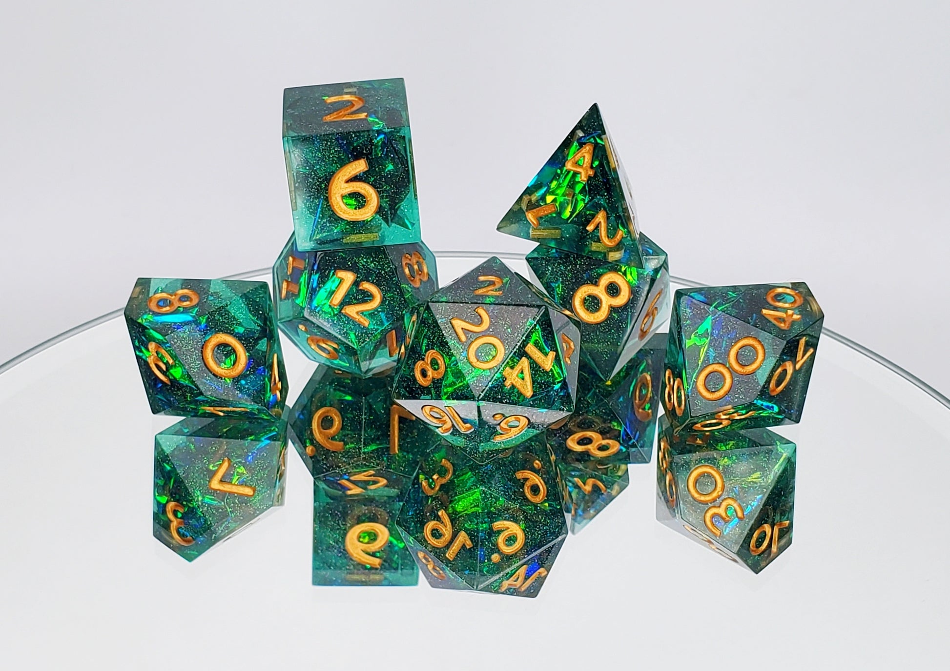 A 7 piece polyhedral dice set arranged on a mirror against a white background. The dice are a transparent green with reflective mylar embedded inside with super fine green glitter throughout and golden numbers.