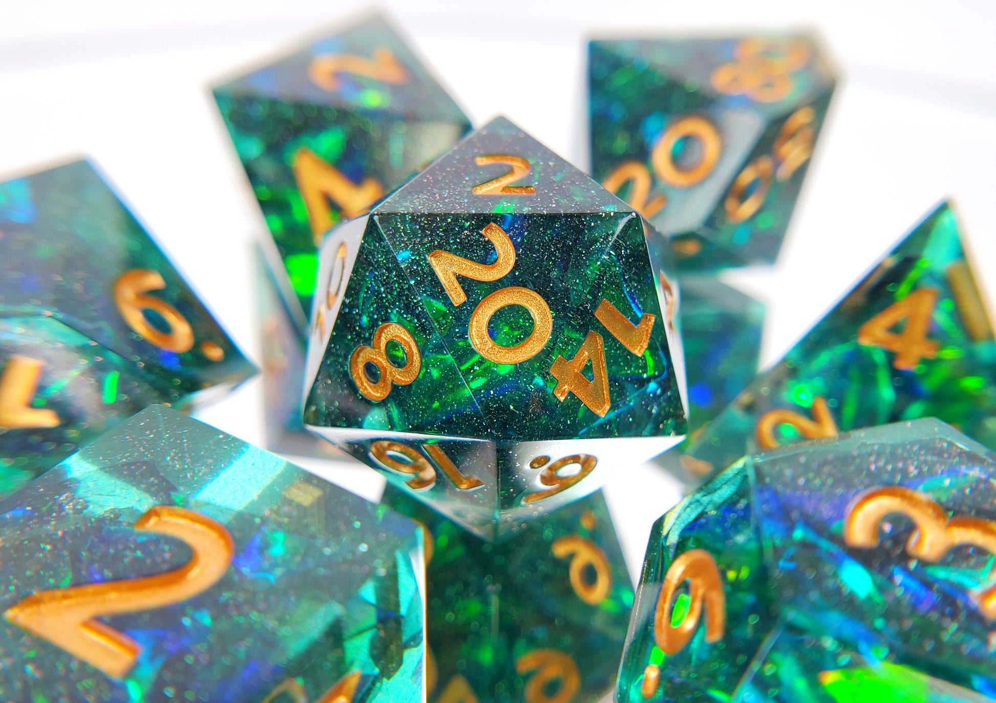 Closeup of a d20, surrounded by the rest of the polyhedral set. The dice are a transparent green with reflective mylar embedded inside with super fine green glitter throughout and golden numbers.