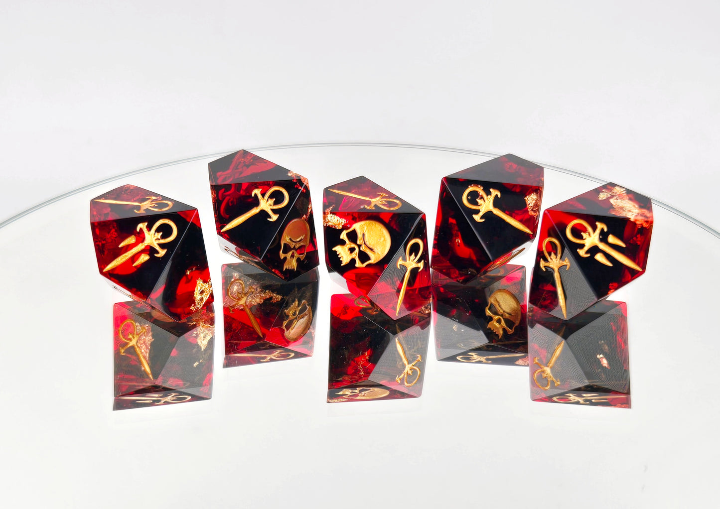 A set of 5 Vampire the Masquerade Hunger style dice. The dice are transparent red with black ink and gold foil inside. The symbols are inked in gold.