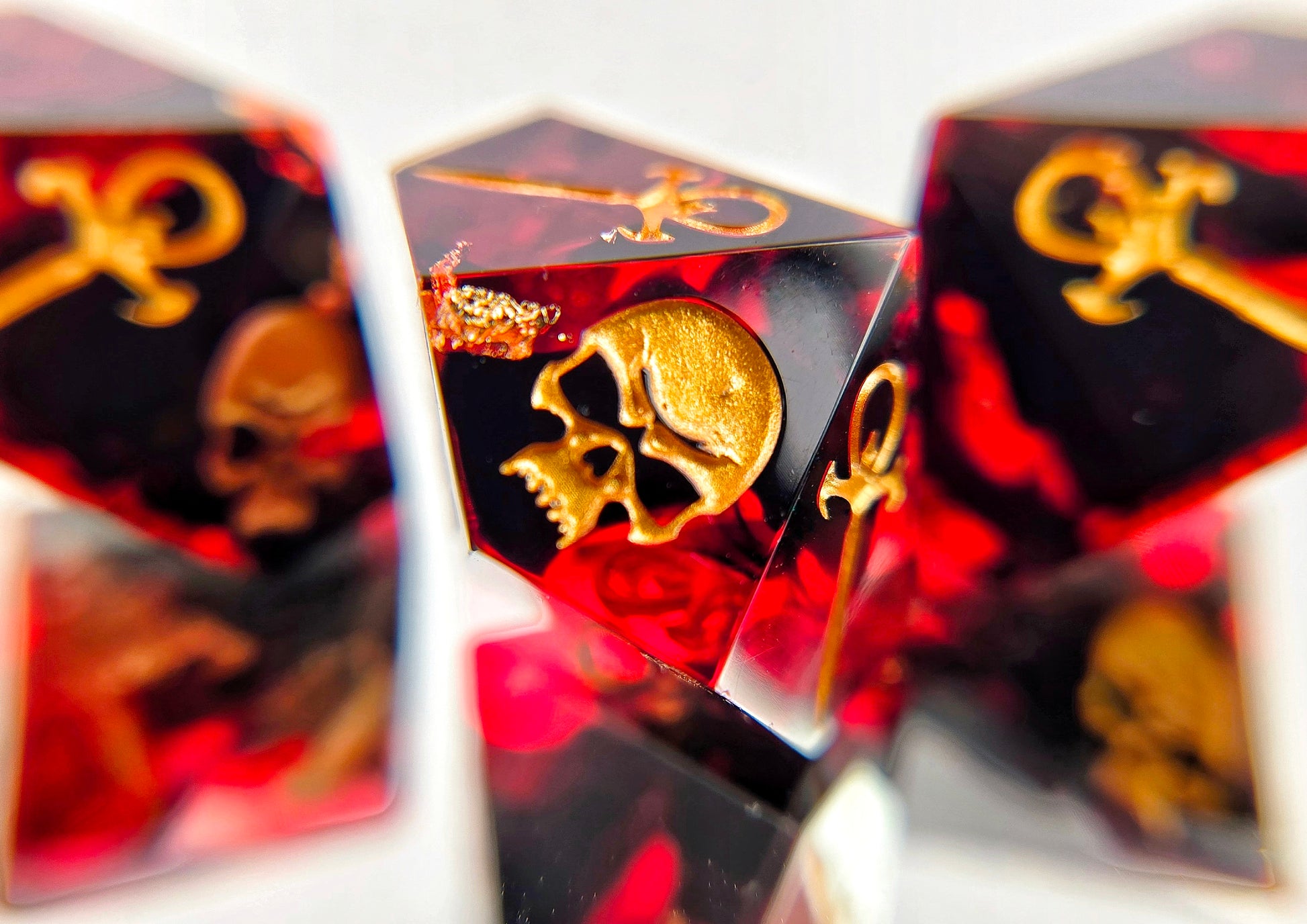 A closeup of a Vampire the Masquerade Hunger style die focusing on the skull. The dice are transparent red with black ink and gold foil inside. The symbols are inked in gold.