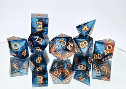 A full 7 piece polyhedral ttrpg dice set. The dice are transparent dark blue with bloops of shimmery silver inside and streaks of bronze coloring across the surface and warm copper numbering. 