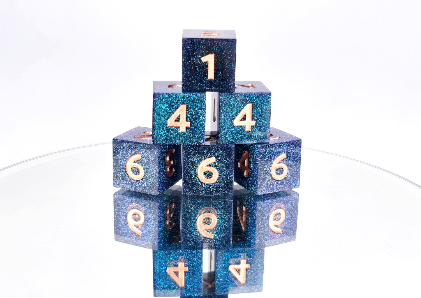 A stack of 6 d6 dice. The dice are densely packed blue and green colorshift glitter with rose gold inking for the symbols.