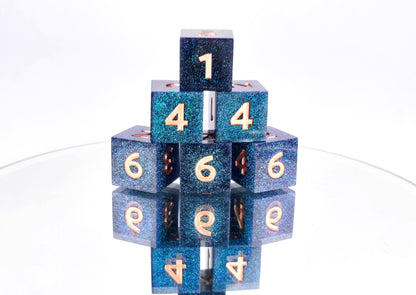 A stack of 6 d6 dice. The dice are densely packed blue and green colorshift glitter with rose gold inking for the symbols.