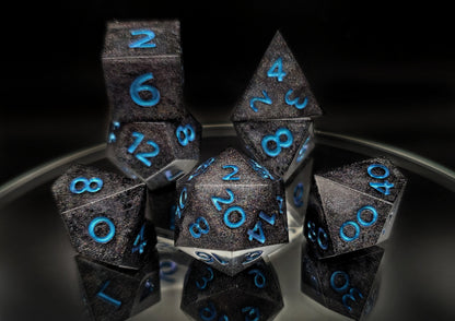 A full 7 piece polyhedral ttrpg dice set. The dice are packed with fine rainbow holographic glitter and bright blue numbers with a mild colorshift to purple visible at the edges of some numbers.