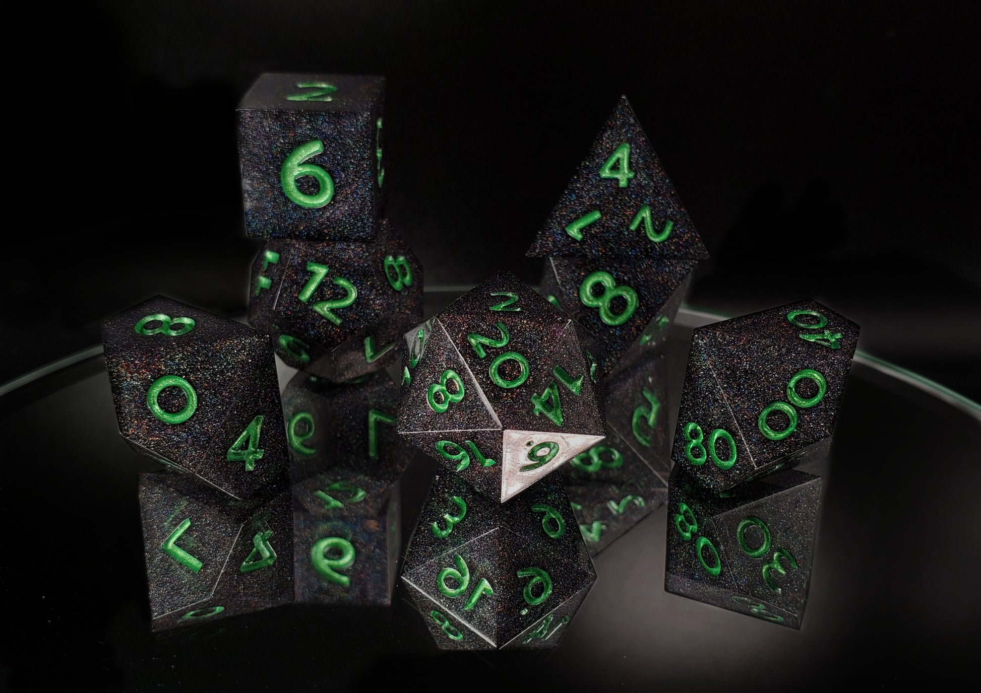 A full 7 piece polyhedral ttrpg dice set. The dice are packed with fine rainbow holographic glitter and green metallic numbers.