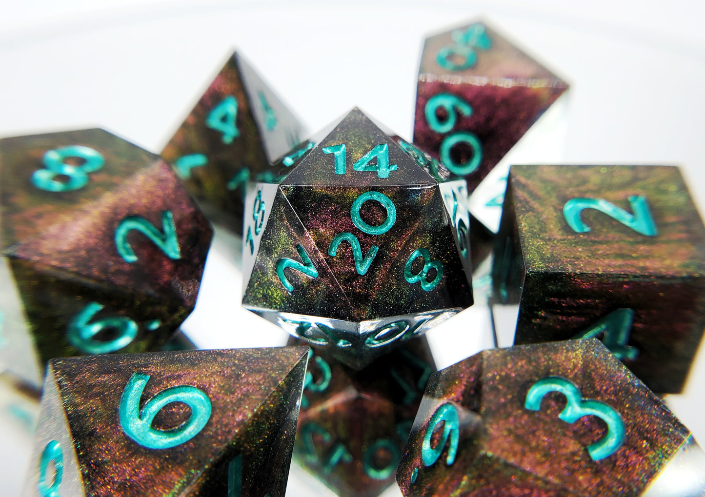 A full 7 piece polyhedral ttrpg dice set. The dice are a red/purple/yellow/green colorshift shimmer with metallic cool green numbering. 